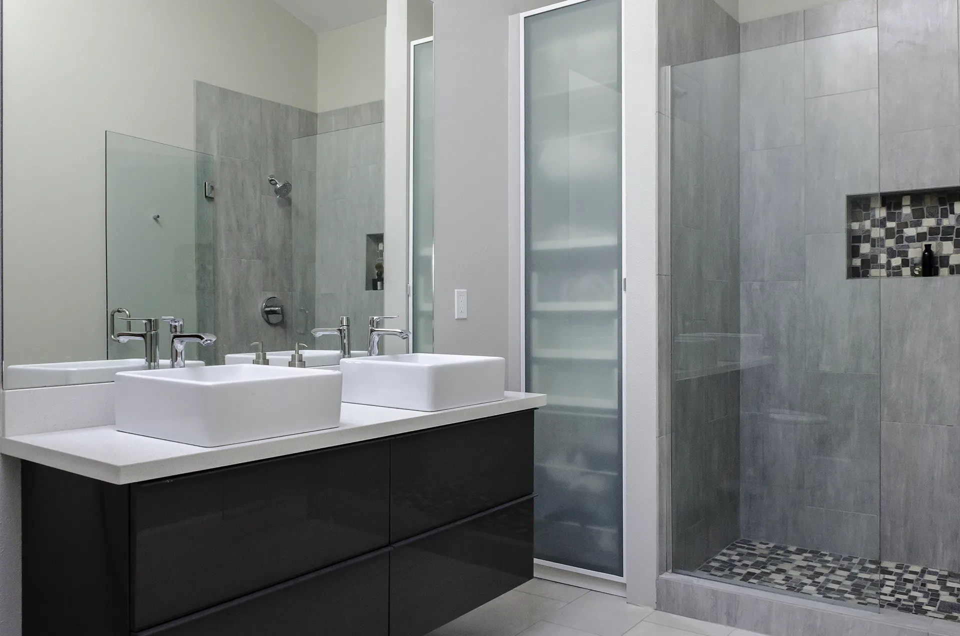 Kirkland master bathroom remodel with double vessel sinks, dark vanity, glass shower door, and mosaic tile accent