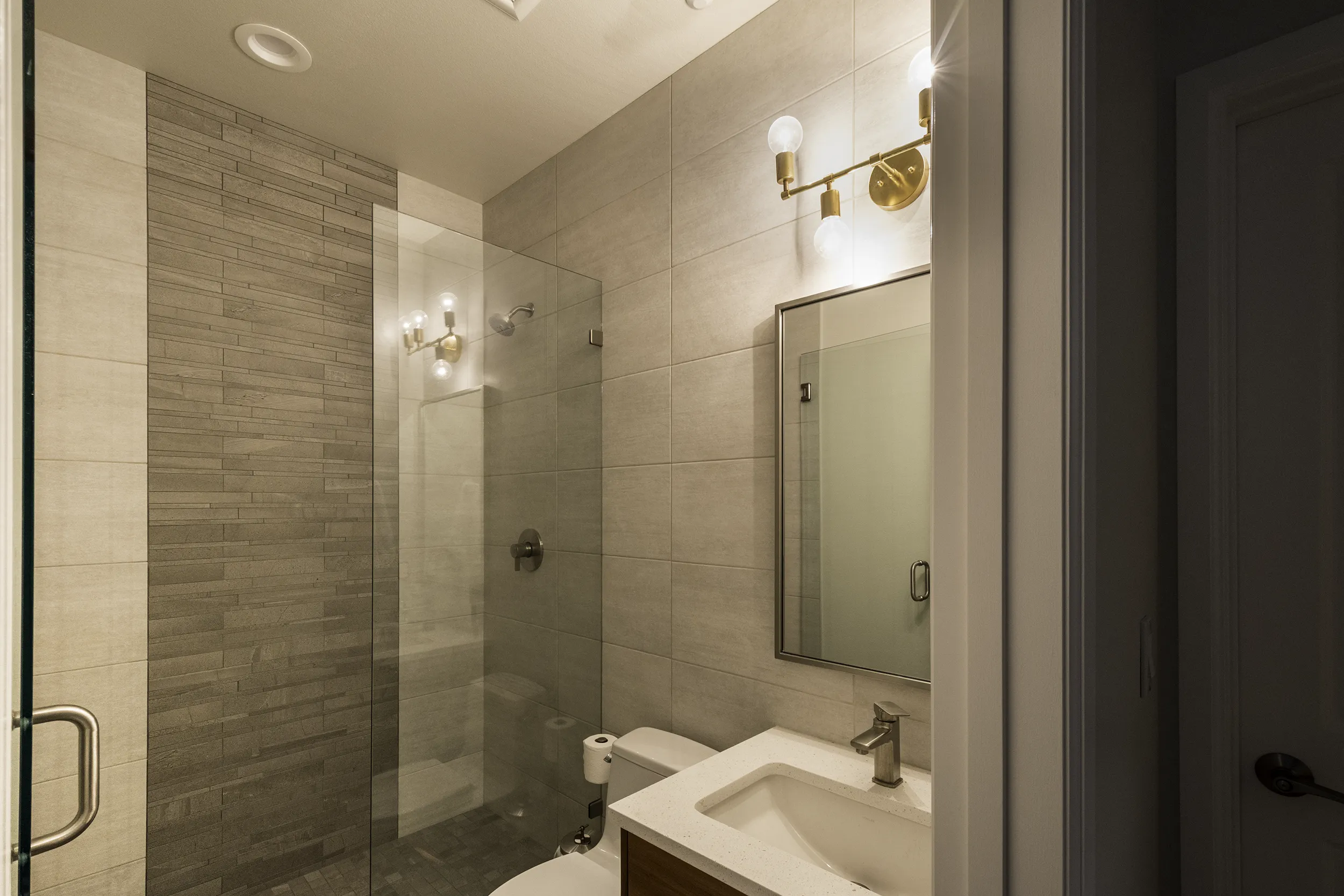 Guest bathroom walk-in shower with frameless glass door and brass sconces