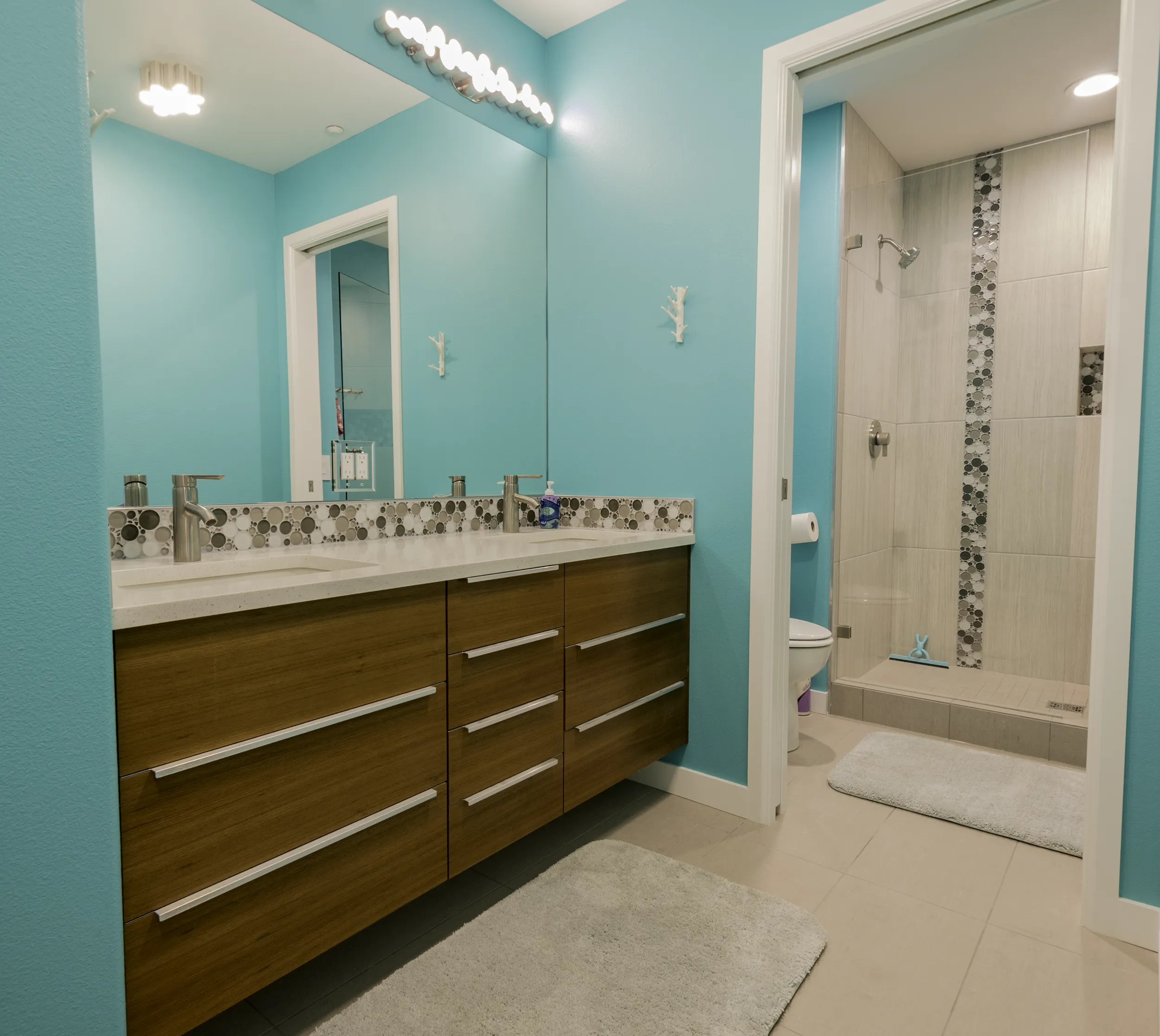 Kids bathroom with teal walls, floating teak vanity, and walk-in shower with bubble mosaic accent
