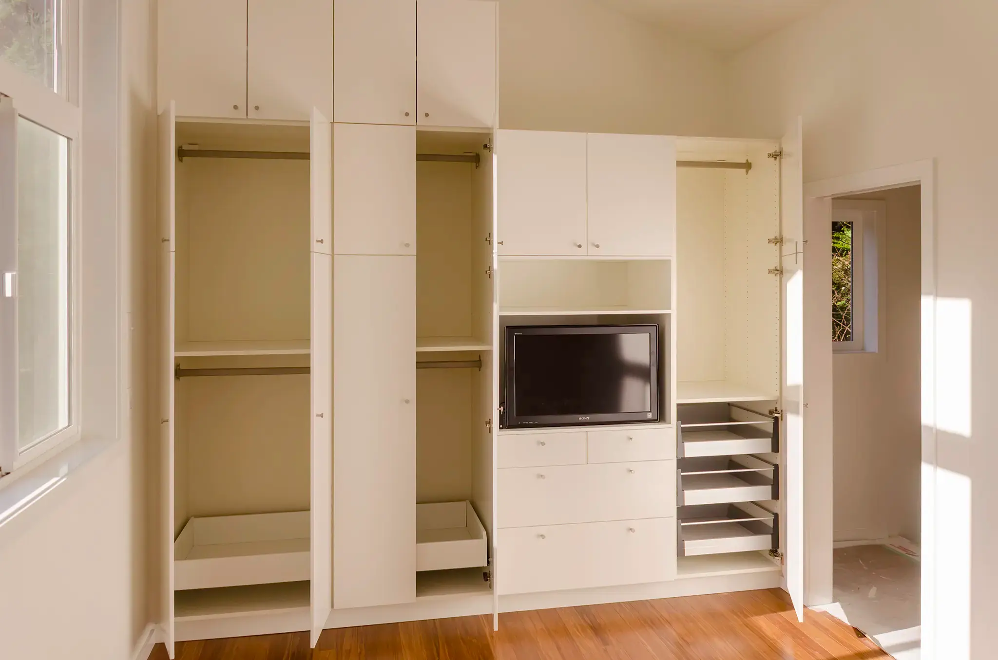 Bedroom wardrobe closet shown open with double hanging rods, drawers and pull-out shoe racks