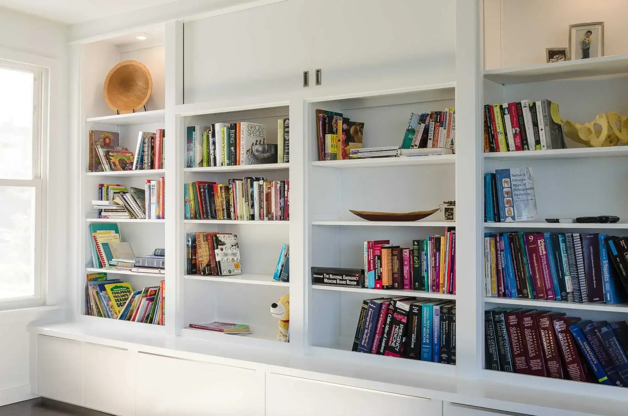 Built-in bookshelves running wall to wall in white, with closed base cabinets underneath