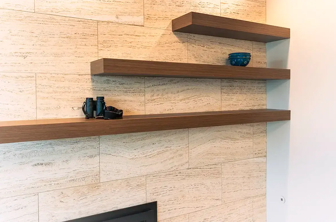 Custom walnut floating shelves mounted over honed travertine tile with no visible brackets