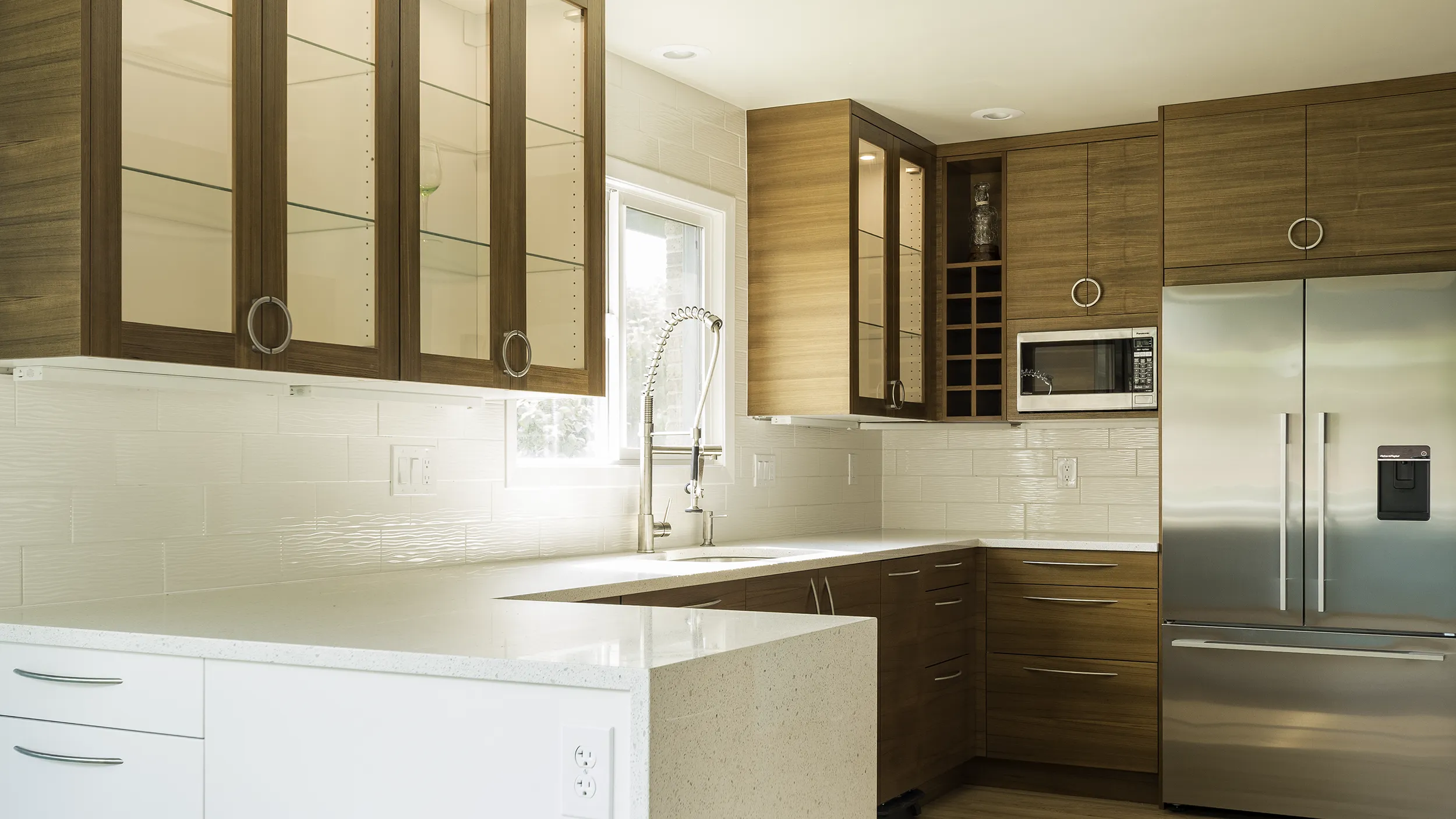Completed IKEA kitchen remodel with wood-tone cabinets, glass-front uppers, white subway tile backsplash, and quartz countertops