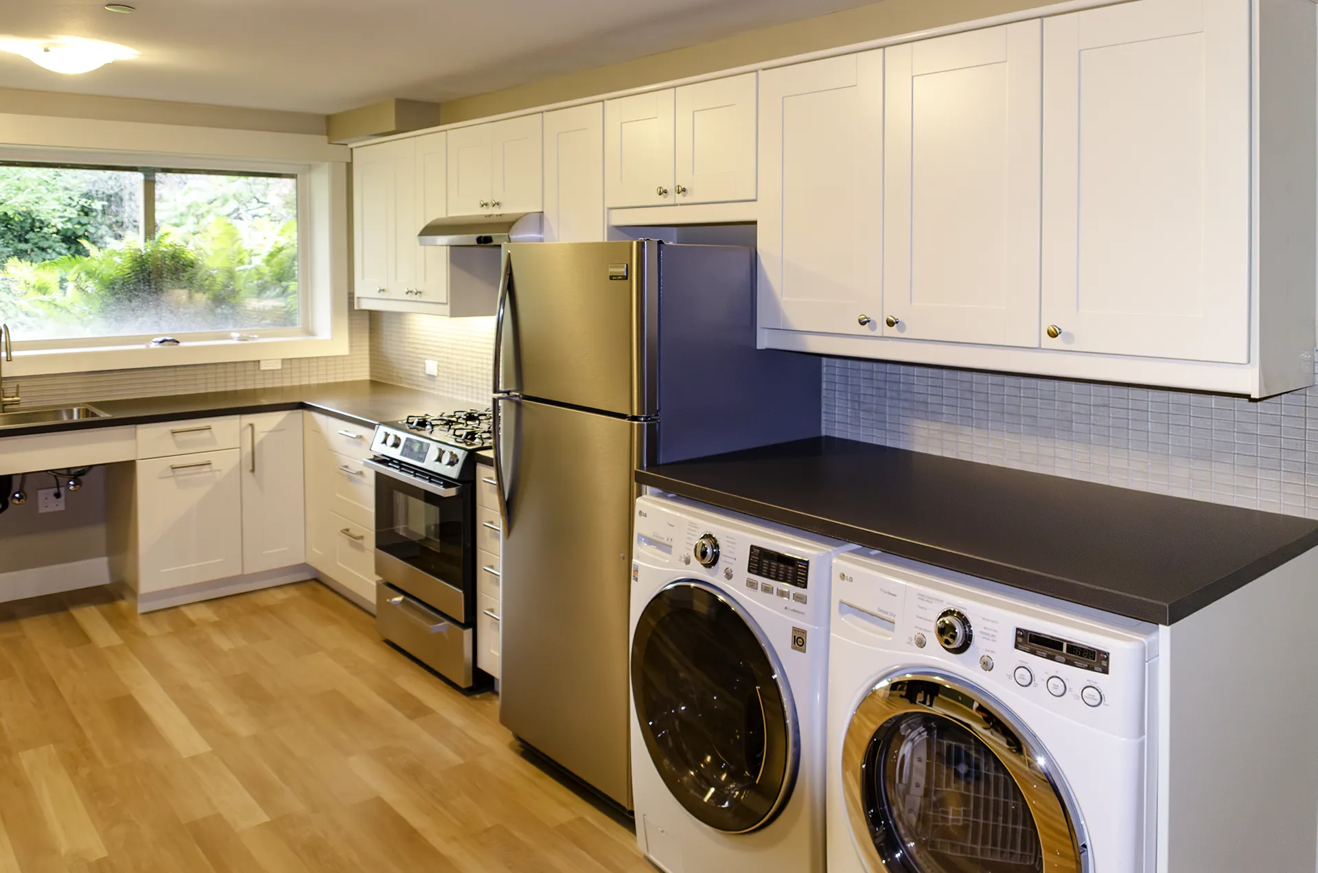 Finished basement kitchenette in Normandy Park with white shaker cabinets, full-size appliances, and a stacked washer-dryer unit