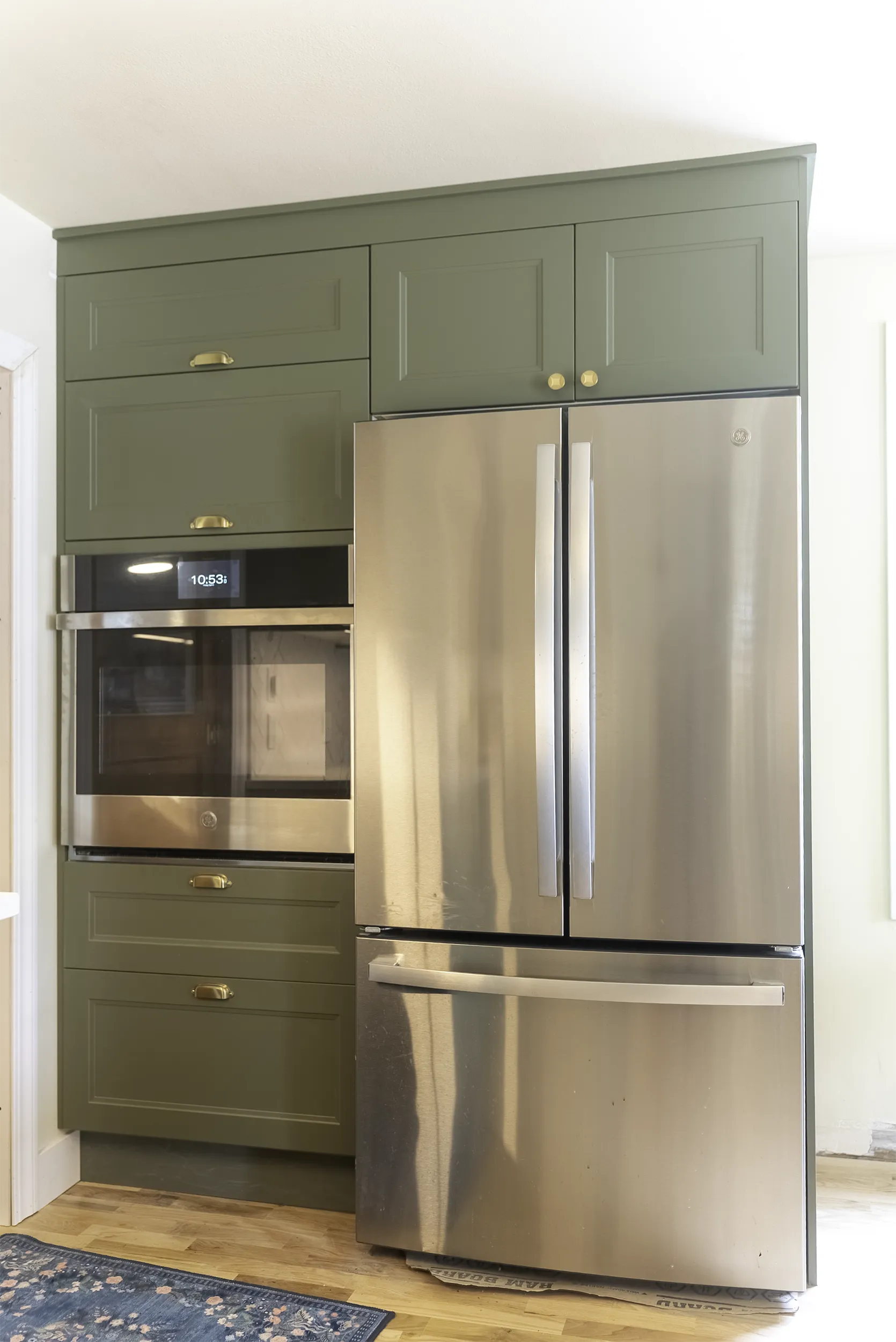 Built-in wall oven and refrigerator framed by green cabinets in a West Seattle kitchen remodel